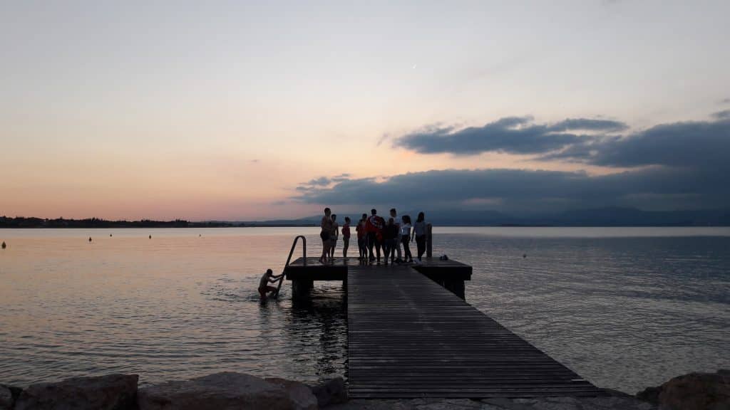 Gruppe von Menschen auf einem Steg bei Sonnenuntergang am Wasser.