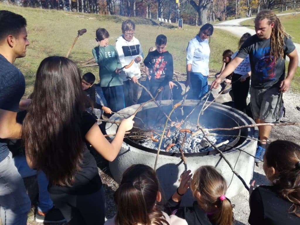 Gruppe von Kindern am Lagerfeuer mit Stöcken zum Grillen.